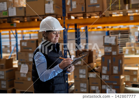 Elderly warehouse manager or supervisor reading document in clipboard. 142807777