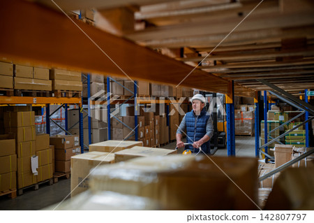 Older male warehouse worker pulling a pallet truck. Older male warehouse worker pulling a pallet truck. 142807797
