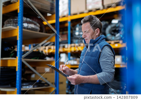 Older warehouse worker working looking at document in clipboard. Older warehouse worker working looking at document in clipboard. 142807809