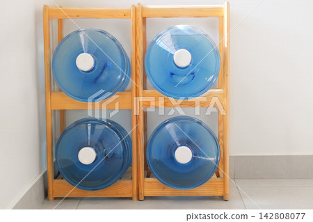 Large drinking water containers are stored on a wooden rack. Water supply. Office water bottles. HDPE bottle. Large drinking water containers are stored on a wooden rack. Water supply. Office water bottles. HDPE bottle. 142808077