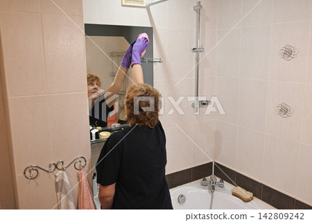 Woman cleaning bathtub in bathroom during afternoon Woman cleaning bathtub in bathroom during afternoon 142809242