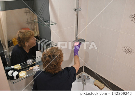 Woman cleaning bathtub in bathroom during afternoon Woman cleaning bathtub in bathroom during afternoon 142809243
