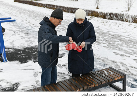 Couple enjoying warm drinks together in winter park while snow covers the ground Couple enjoying warm drinks together in winter park while snow covers the ground 142809267