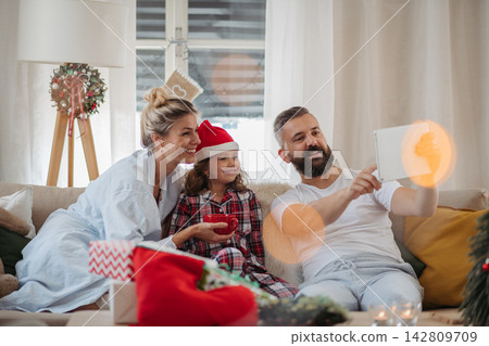 Family watching Christmas movie together on tablet during cozy holiday at home. 142809709