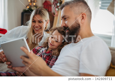 Family watching Christmas movie together on tablet during cozy holiday at home. Family watching Christmas movie together on tablet during cozy holiday at home. 142809711