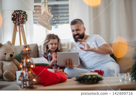 Dad and daughter waving to relatives during virtual Christmas celebration from home. Dad and daughter waving to relatives during virtual Christmas celebration from home. 142809716