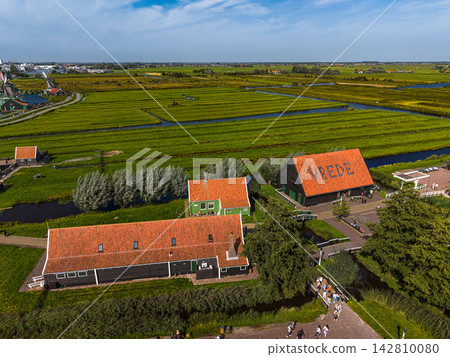 High angle wide horizontal aerial drone photograph of Zaanse Schans historic Vrede barn, green wooden houses, red tiled roofs, polder canals, and windmills in Zaandam, North Holland, Netherlands High angle wide horizontal aerial drone photograph of Zaanse Schans historic Vrede barn, green wooden houses, red tiled roofs, polder canals, and windmills in Zaandam, North Holland, Netherlands 142810080