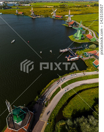 High angle vertical aerial drone photograph of Zaanse Schans historic windmills, river Zaan, ferry dock pier, green polder canals, and walking path in Zaandam, North Holland, Netherlands on day High angle vertical aerial drone photograph of Zaanse Schans historic windmills, river Zaan, ferry dock pier, green polder canals, and walking path in Zaandam, North Holland, Netherlands on day 142810087