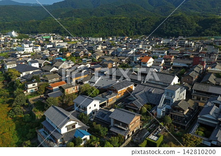 一張空拍照片，展現了德島縣美間市的城鎮風貌，包括瓦片屋頂和白色牆壁。 142810200