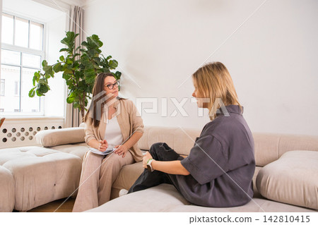 Psychologist talking with woman patient in office. Professional therapy session sitting on sofa. Mental health treatment, support consultation and counseling concept interior. Psychologist talking with woman patient in office. Professional therapy session sitting on sofa. Mental health treatment, support consultation and counseling concept interior. 142810415