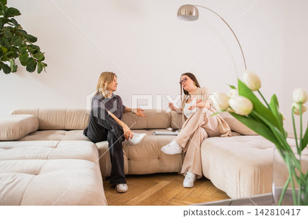 Woman psychologist talking with a woman client sitting on a sofa during a therapy session. Professional mental health consultation in a cozy office. Support and psychotherapy concept. 142810417