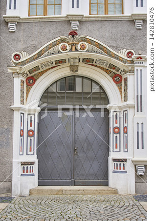 Large gray metal door set in ornate arched entrance with painted decorative details Large gray metal door set in ornate arched entrance with painted decorative details 142810476