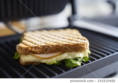 Sandwich with cheese, deli meat and lettuce cooking on electric grill Sandwich with cheese, deli meat and lettuce cooking on electric grill 142810480