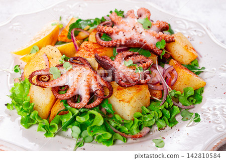 Grilled octopus with baked potatoes and fresh herbs, on a decorative light plate, homemade, no people Grilled octopus with baked potatoes and fresh herbs, on a decorative light plate, homemade, no people 142810584