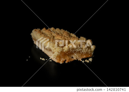 Delicious slice of traditional German apple crumble cake isolated on black background. Perfect stock photo for bakery menus, coffee shop ads, and dessert posters. Delicious slice of traditional German apple crumble cake isolated on black background. Perfect stock photo for bakery menus, coffee shop ads, and dessert posters. 142810741
