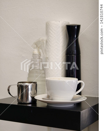 A white coffee cup and a milk jug on a shelf in a cafe. A white coffee cup and a milk jug on a shelf in a cafe. 142810744