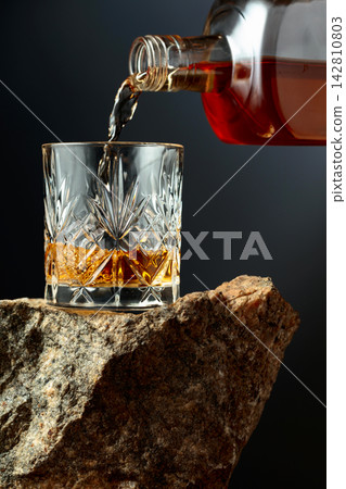 Whiskey is poured from a bottle into a glass. Whiskey is poured from a bottle into a glass. 142810803