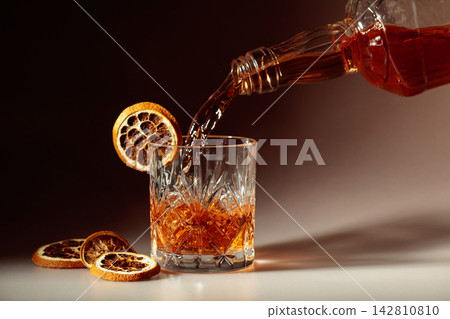 Whiskey is poured into a in crystal glass garnished with dried orange slices. 142810810