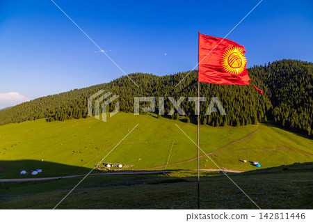 Serene landscape with tents and livestock in Kyrgyzstan under damaged national flag Serene landscape with tents and livestock in Kyrgyzstan under damaged national flag 142811446