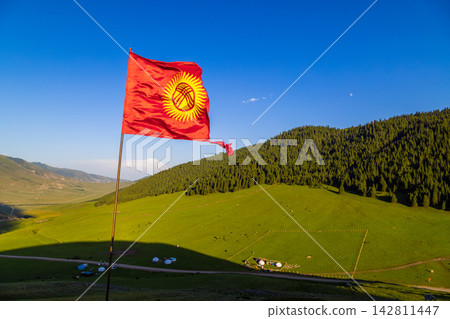Kyrgyzstan valley with tattered national flag, yurts and grazing animals Kyrgyzstan valley with tattered national flag, yurts and grazing animals 142811447