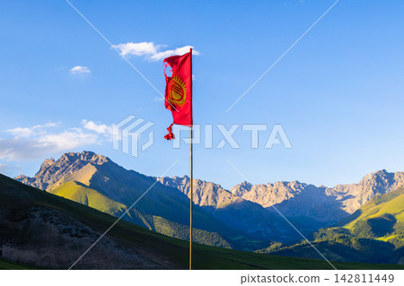 Torn National Flag of Kyrgyzstan on pole against mountains and sky at summer evening Torn National Flag of Kyrgyzstan on pole against mountains and sky at summer evening 142811449