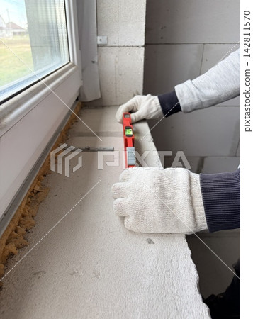 Construction and renovation concept. A man uses a metal spirit level to check the quality of the work performed. Construction and renovation concept. A man uses a metal spirit level to check the quality of the work performed. 142811570