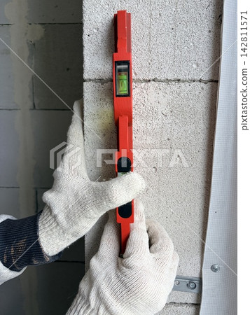 A man uses a metal level to check the straightness of the walls. A man uses a metal level to check the straightness of the walls. 142811571