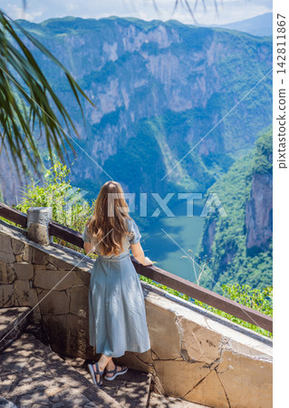 Woman tourist admiring the dramatic Sumidero Canyon viewpoint in Chiapas Mexico with steep canyon walls lush landscape river overlook nature tourism and posing at the observation area. Woman tourist admiring the dramatic Sumidero Canyon viewpoint in Chiapas Mexico with steep canyon walls lush landscape river overlook nature tourism and posing at the observation area. 142811867