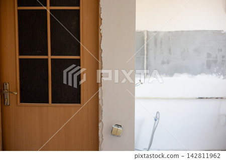 Interior renovation with wood door, unfinished plaster around the doorway, exposed wiring and a partly fitted wall switch, showing major construction, repair and home improvement work is now underway. 142811962