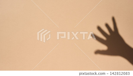 Shadow of a human hand with spread fingers on a light beige background. Shadow of a human hand with spread fingers on a light beige background. 142812083