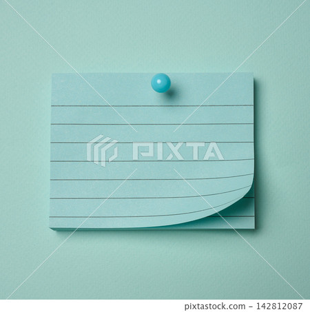 Lined notepad sheet with a curled edge pinned on a blue background. Lined notepad sheet with a curled edge pinned on a blue background. 142812087