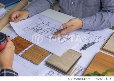 An architect or interior designer is reviewing floor plans with a client to finalize design details. An architect or interior designer is reviewing floor plans with a client to finalize design details. 142812193
