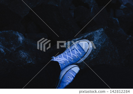 Blue canvas sneakers resting on dark rocks in dramatic low light, creating a moody fashion image with cool monochromatic tones, outdoor lifestyle styling and a bold contemporary aesthetic for branding Blue canvas sneakers resting on dark rocks in dramatic low light, creating a moody fashion image with cool monochromatic tones, outdoor lifestyle styling and a bold contemporary aesthetic for branding 142812284