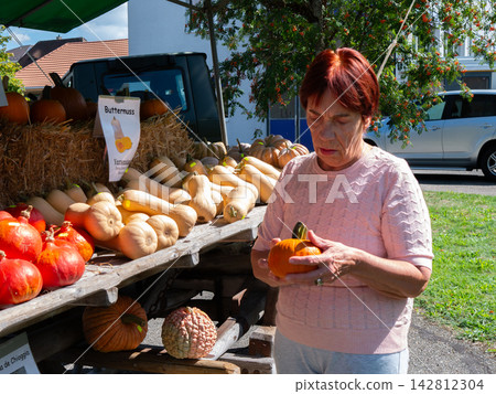 Pumpkin exhibition and autumn season farmers market where a woman is choosing a small gourd from the display stand Pumpkin exhibition and autumn season farmers market where a woman is choosing a small gourd from the display stand 142812304
