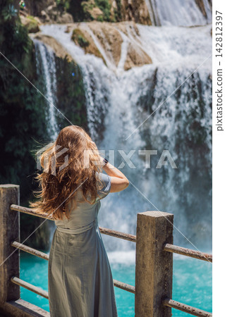 Woman traveler admiring El Chiflon waterfall from a wooden viewpoint in Chiapas Mexico with wooden railings tropical forest clear blue water nature travel and looking at the waterfall. 142812397