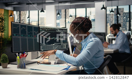 Equity analyst in prop firm office reviews quarterly earnings to assess future stock market value, taking notes. Trader conducts financial analysis to improve investments, writing down info Equity analyst in prop firm office reviews quarterly earnings to assess future stock market value, taking notes. Trader conducts financial analysis to improve investments, writing down info 142812847