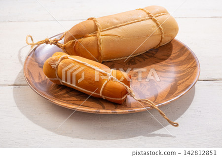 Provolone cheese, some smoked provolone cheeses made in Brazil placed on a ceramic plate, on rustic white wood, selective focus. 142812851