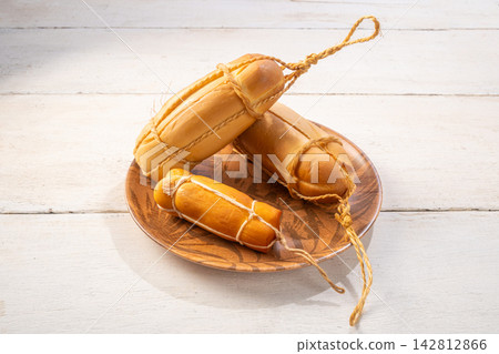 Provolone cheese, some smoked provolone cheeses made in Brazil placed on a ceramic plate, on rustic white wood, selective focus. Provolone cheese, some smoked provolone cheeses made in Brazil placed on a ceramic plate, on rustic white wood, selective focus. 142812866