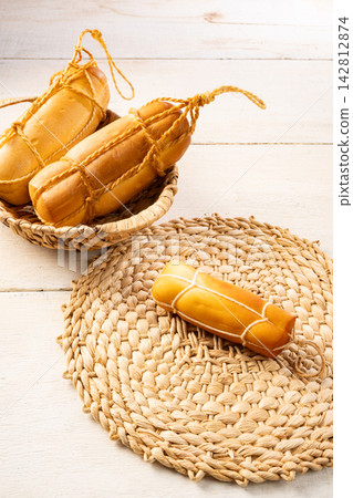 Provolone cheese, Some smoked provolone cheeses made in Brazil placed on straw utensils, on rustic white wood, selective focus. Provolone cheese, Some smoked provolone cheeses made in Brazil placed on straw utensils, on rustic white wood, selective focus. 142812874