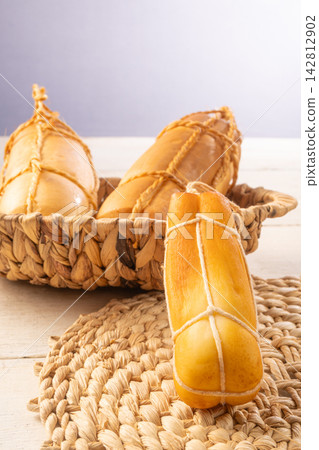 Provolone cheese, Some smoked provolone cheeses made in Brazil placed on straw utensils, on rustic white wood, selective focus. 142812902