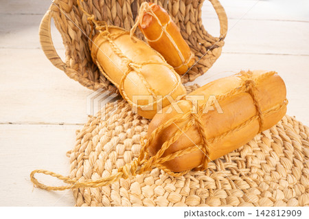 Provolone cheese, Some smoked provolone cheeses made in Brazil placed on straw utensils, on rustic white wood, selective focus. Provolone cheese, Some smoked provolone cheeses made in Brazil placed on straw utensils, on rustic white wood, selective focus. 142812909