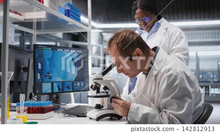 Employees team studying sample tray under the microscope for research study in a lab, cellular investigation and supporting genetics research. Advanced analysis for healthcare. Employees team studying sample tray under the microscope for research study in a lab, cellular investigation and supporting genetics research. Advanced analysis for healthcare. 142812913