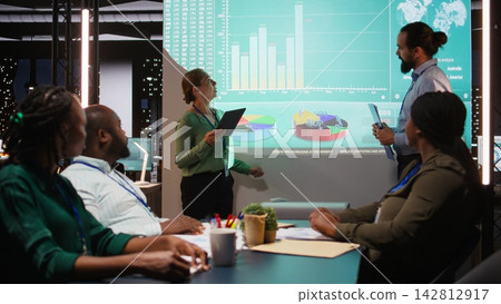 Diverse staff from an enterprise sharing data analytics and insights for a new project agenda during late night corporate meeting. Workers discuss about resources allocation. Camera A. Diverse staff from an enterprise sharing data analytics and insights for a new project agenda during late night corporate meeting. Workers discuss about resources allocation. Camera A. 142812917