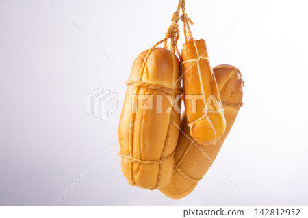 Provolone cheese, some smoked provolone cheeses made in Brazil hanging from ropes, white background, selective focus. Provolone cheese, some smoked provolone cheeses made in Brazil hanging from ropes, white background, selective focus. 142812952