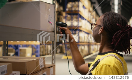 Black e-commerce employee scanning awb tracking numbers, registering shipping labels and details for the warehouse inventory records. Handling pallets import export operations. Camera A. Black e-commerce employee scanning awb tracking numbers, registering shipping labels and details for the warehouse inventory records. Handling pallets import export operations. Camera A. 142812976