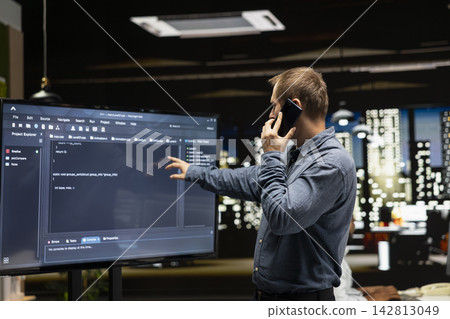 Manager in startup office calling IT department workers after noticing error in code on monitor. Team leader making phone call, concerned by mistakes in programming language on large screen Manager in startup office calling IT department workers after noticing error in code on monitor. Team leader making phone call, concerned by mistakes in programming language on large screen 142813049