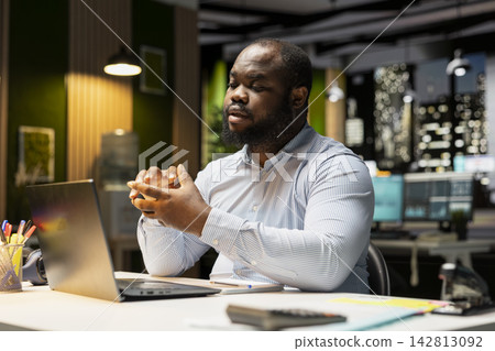 African american guy participates in a virtual web call to address business issues, speaking confidently on laptop late at night. Young man making an internet connection with shareholders. 142813092