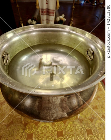 A silver baptismal font with water and an Orthodox cross. A silver baptismal font with water and an Orthodox cross. 142813280