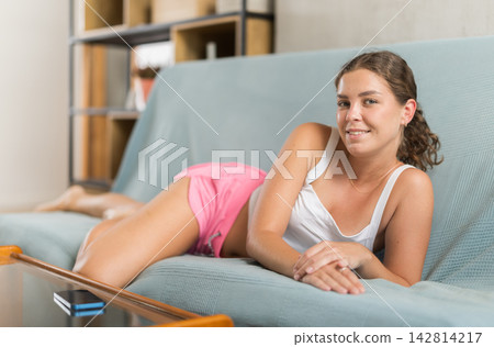 Young girl wearing summer shorts lying on sofa Young girl wearing summer shorts lying on sofa 142814217