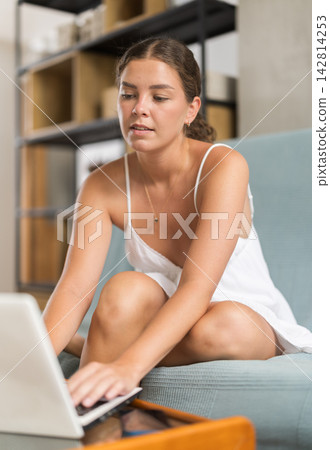 Young woman working on laptop sitting on sofa Young woman working on laptop sitting on sofa 142814253